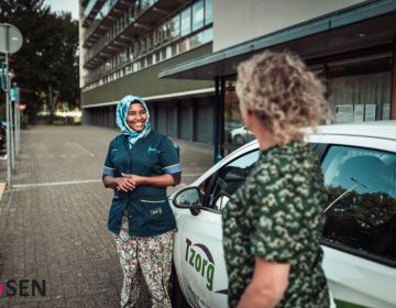 Zorgmedewerker en vrouw staan naast een auto en lachen naar elkaar