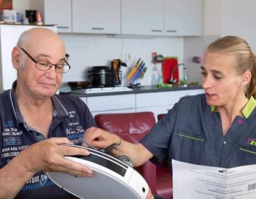 Medewerkster van tzorg legt oudere man uit hoe de stofzuiger werkt.