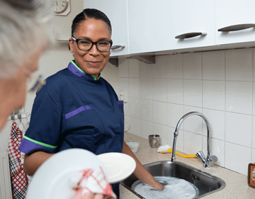 Zorgmedewerker helpt oudere met afwassen