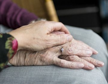 Close-up van twee handen, waarbij een jongere hand liefdevol een ouder hand vasthoudt.