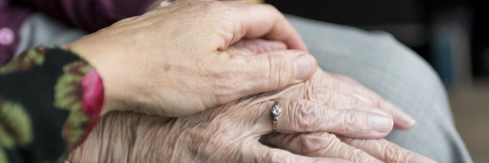 Close-up van twee handen, waarbij een jongere hand liefdevol een ouder hand vasthoudt.